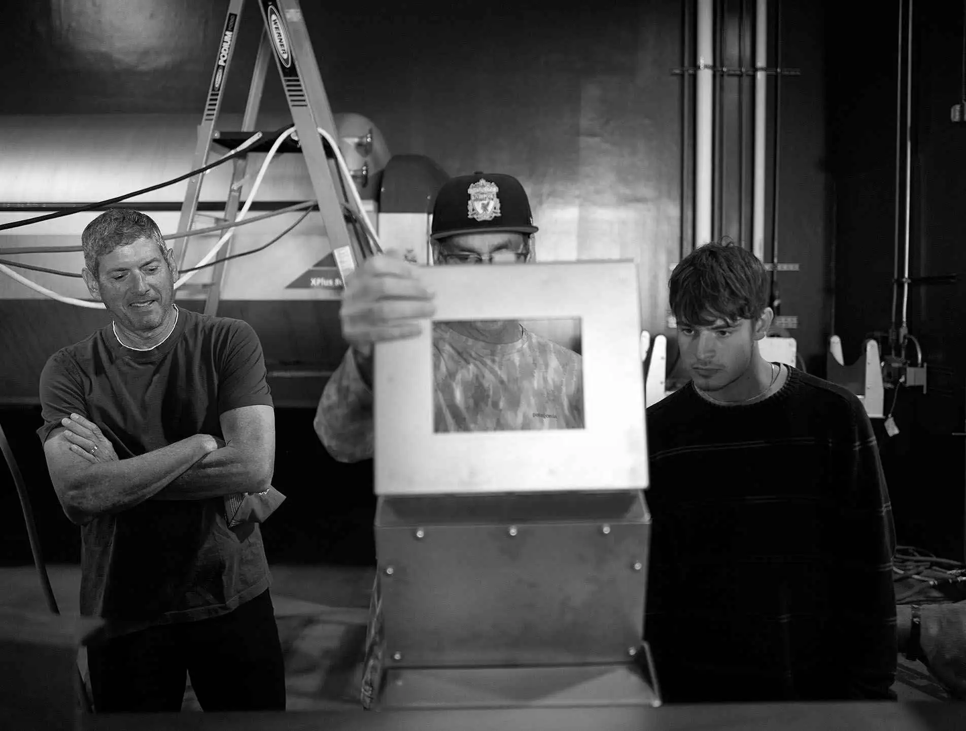 Three men look at a metal project in a workshop.